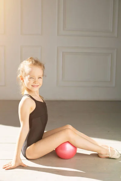 Petite fille en maillot de bain noir s'assoit magnifiquement contre la fenêtre avec boule rose — Photo