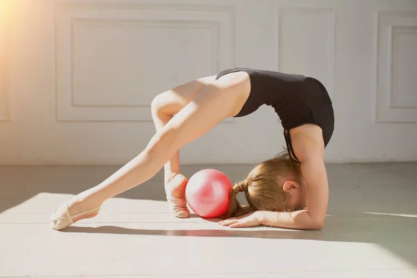 En liten gymnast i svart trikå gjorde gymnastikträning. Den unga flickan böjer ryggen och står på hans huvud och ben. — Stockfoto