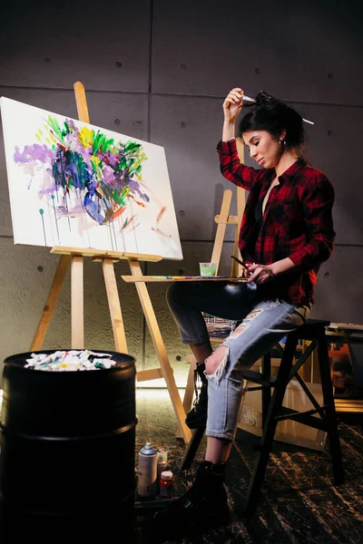 Attractive brunette at home artist paints on an easel with watercolors during the quarantine due to coronavirus infection.