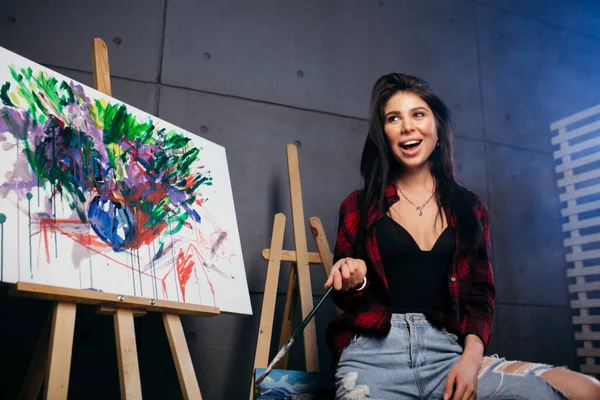 El artista en una camisa a cuadros roja con un pincel en las manos se regocija por el hecho de que terminé una pintura colorida abstracta . — Foto de Stock