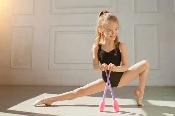 Bella giovane ginnasta fa esercizi con aste rosa ginnastica. Esercizio e stretching per bambini . — Foto Stock