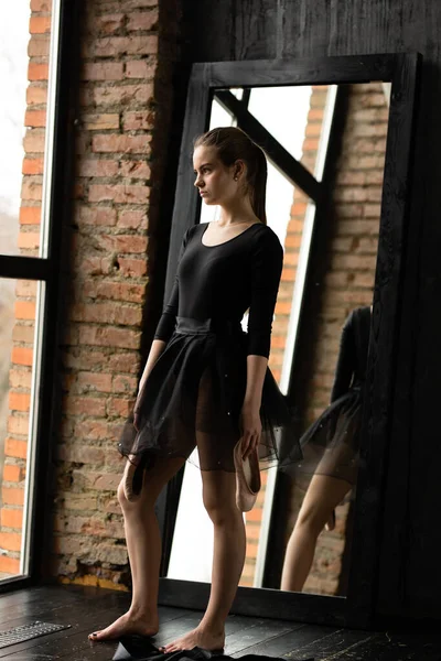 한 젊은 발레리나 는 손에 점을 들고 서서 장시간 일 한 후에 쉬고 있다. 창문 과 거울을 배경으로. — 스톡 사진