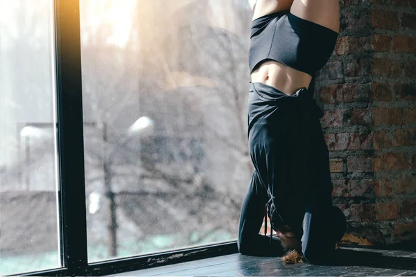 Pelatih Pilates melakukan handstand dekat dinding bata. Gadis sporty dalam pakaian hitam menarik kaki ke atas — Stok Foto