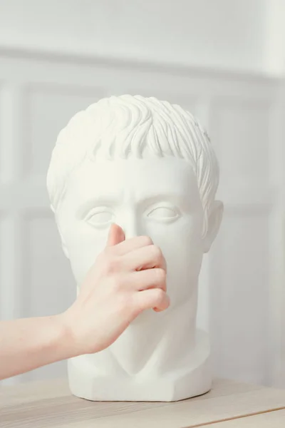 Female hand pokes a finger into the nose of Gypsum sculpture of Caesar's head. Head stands on a wooden table in a classic interior — Stock Photo, Image