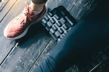 Vücut masajı için yakın çekim siyah masaj silindiri. Yoga ve pilates için spor malzemeleri. Pembe spor ayakkabılar ve siyah taytlar.