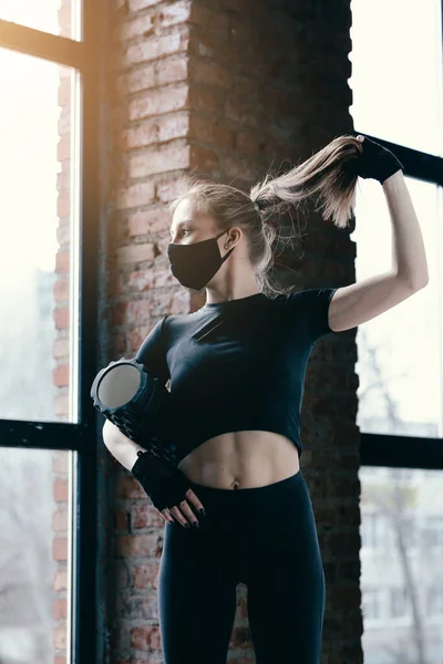 Vacker smal profil av en vältränad flicka. Yoga trainer med svart massagerulle bandage svans under ett träningspass mot ett fönster. — Stockfoto