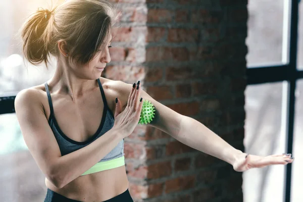 Um treinador de ioga jovem em um tópico curto está trabalhando os músculos do braço com uma bola miofascial verde . — Fotografia de Stock