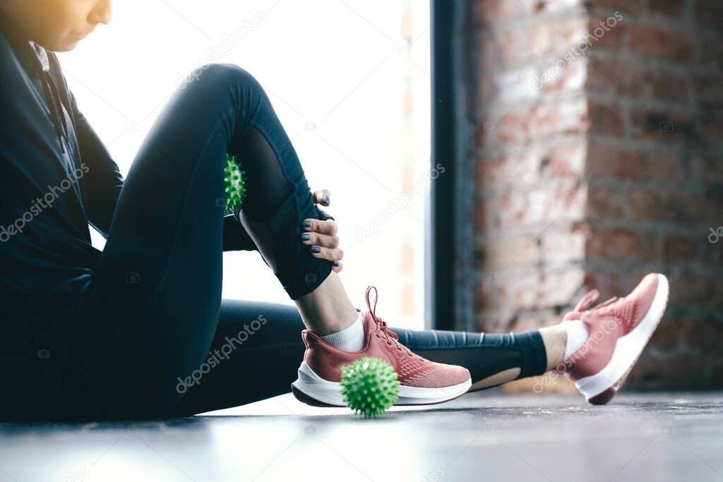 Close-up inflated legs in leggings. The girl leans a hip on the green Ball Myofascial. Massage of the thighs.