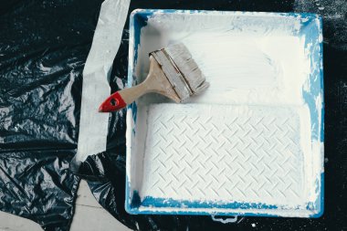 İnşaat paletine beyaz boya dökülüyor. Boya için Cuvette, tamir için fırça, yerde polietilen malzeme..