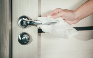 Kadın eli bir bezle kapı kolunu siler. Koronavirüs salgını sırasında yüzey dezenfeksiyonu