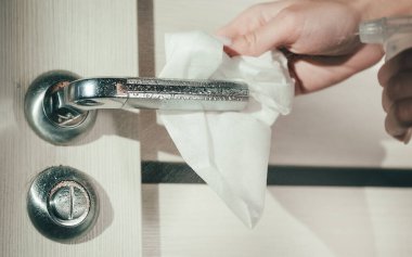 Kadın eli bir bezle kapı kolunu siler. Koronavirüs salgını sırasında yüzey dezenfeksiyonu