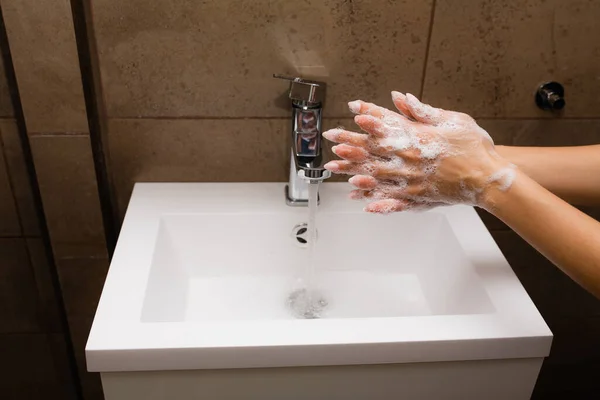 Девушка моет в раковине руки с антибактериальным мылом, чтобы защитить от угрозы коронавирусной инфекции во время самоизоляции — стоковое фото