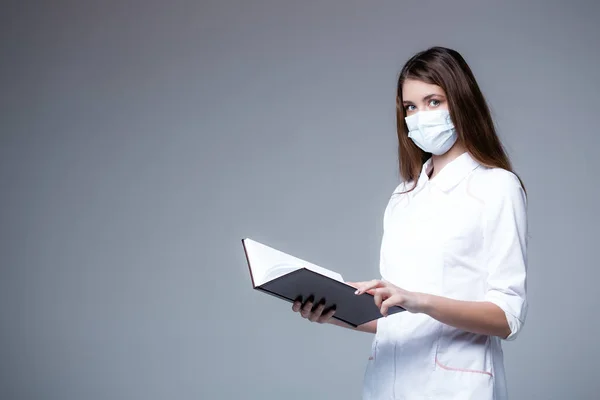 Uma bela garota médica americana em uma máscara médica e um manto branco segurando um calendário em um fundo branco — Fotografia de Stock