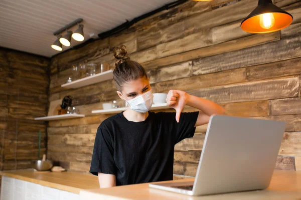 Chica en una máscara médica en la cocina hablando en línea y mostrando los pulgares hacia abajo — Foto de Stock