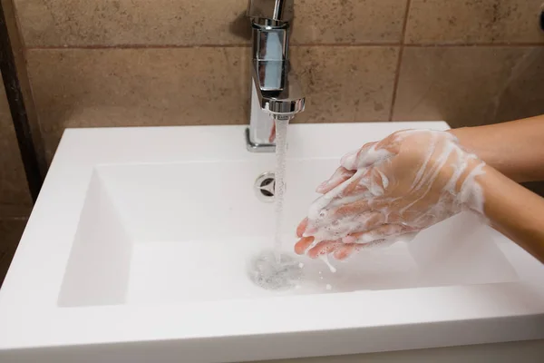 Beyaz bir lavaboda el yıkama. Su, sabunlu kadın ellerine akar. Koronavirüs ve enfeksiyonlara karşı koruma. — Stok fotoğraf