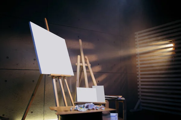 Blanco doek ophangen. Donkere kunst Studio met houten ezels, palet en abstract beeld geschilderd met aquarelverf. — Stockfoto