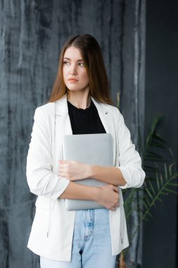 Amerikalı çalışan bir dizüstü bilgisayar tutuyor ve pencereye bakıyor. Karantina sırasında evde çalış.