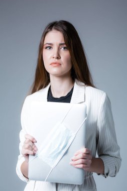 Suratsız bir kız elinde tıbbi maskenin takılı olduğu bir dizüstü bilgisayar tutuyor. Karantina konsepti