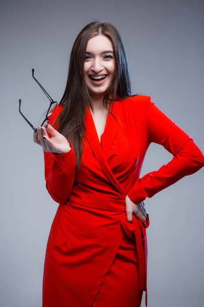 Uma mulher indiana em um vestido vermelho segura óculos perto de seu rosto e ri da câmera. Retrato sessão de fotos de uma mulher de negócios . — Fotografia de Stock