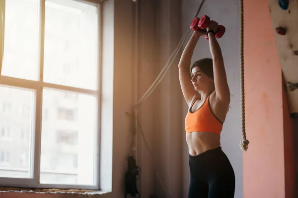 Antrenorul de fitness efectuează exerciții sportive pentru pomparea brațelor. Ţine gantere roşii şi le ridică. — Fotografie, imagine de stoc