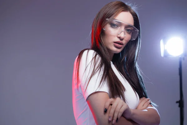 Retrato de una mujer europea con estilo en una camiseta blanca con gafas transparentes y brazos cruzados en el pecho. Luz roja en el fondo . —  Fotos de Stock