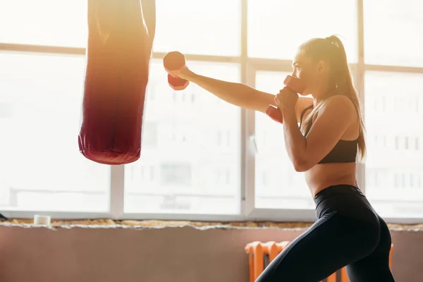 Fitness Boxing trainer girl praticando com um saco de perfuração e bate com halteres nas mãos no salão de artes marciais — Fotografia de Stock