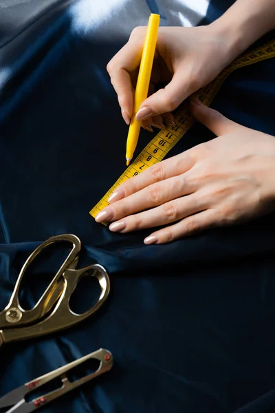 Een close-up. Een naaister maakt markeringen met een potlood en een liniaal op stof. Kleerschaar en een draadschaar liggen op de stof. — Stockfoto