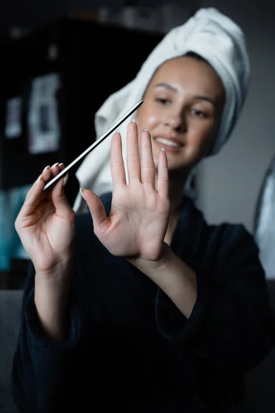 Латиноамериканка делает маникюр с пилкой для ногтей в халате и полотенцем на голове — стоковое фото