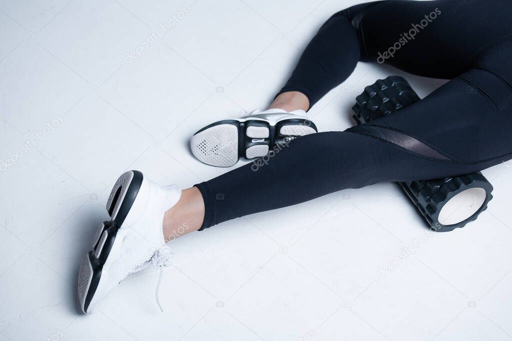 Close-up of female legs. Fitness trainer warms the fascia of the anterior thigh using a massage cylinder on a white background