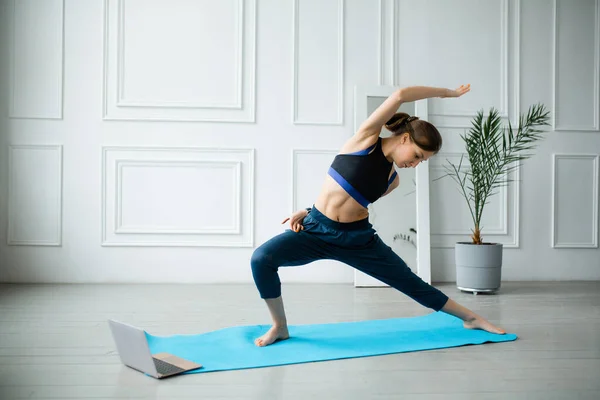 Instructorul de yoga efectuează exerciții online pe un laptop acasă. Exerciții de întindere pentru mușchii spatelui și picioarelor, oblicuri — Fotografie, imagine de stoc