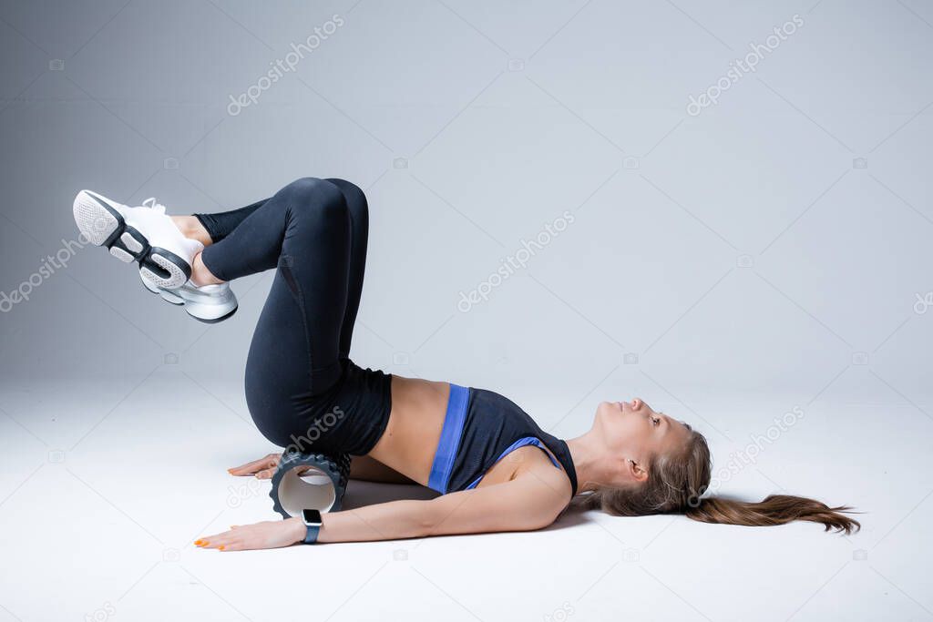 Girl massages muscles of the lower back, lifting his legs up and lying on her back, with sports roller to restore fascia mobility