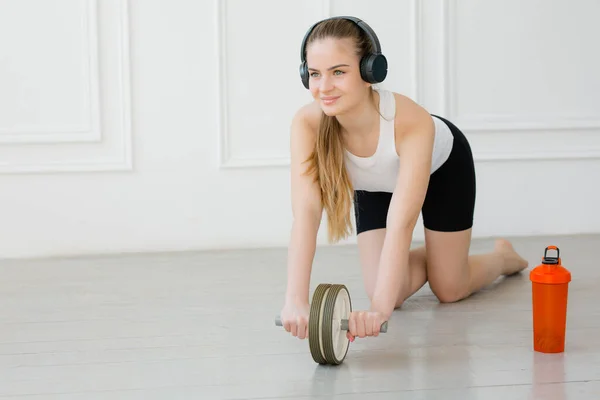 Girl doing exercises with a press roller on the floor in an apartment next to a red water bottle