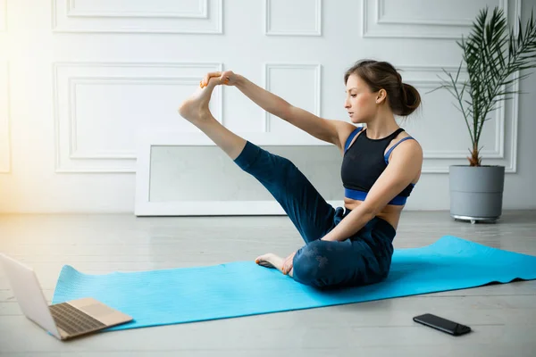 Жінка намагається зробити нові вправи йоги в відеоурок на ноутбуці. Натяжні вправи на спині м'язів ніг — стокове фото