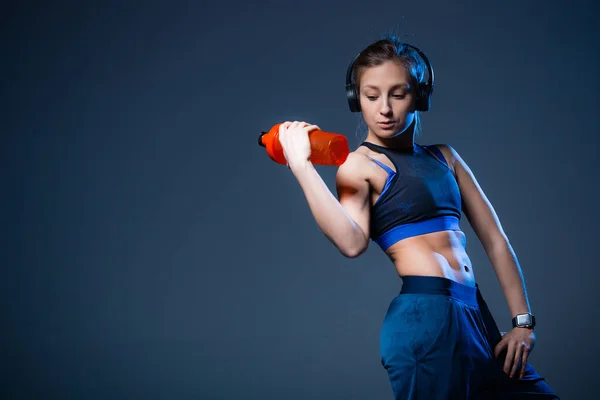 Спортсмен з рельєфним тиском у пошуках пляшки води. Дівчина в навушниках і спортивний синій топ . — стокове фото