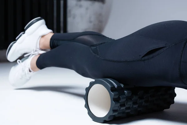 The trainer massages the muscles of the hips and legs, anterior thigh muscle before starting training with a black massage roller.