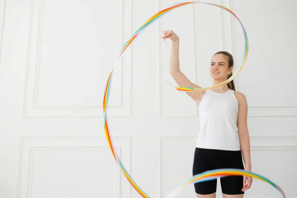Jeune fille athlète se tient dans un studio lumineux sur un fond blanc et effectue un exercice cercles ruban de gymnastique — Photo