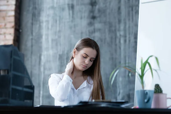 Una chica europea cansada masajea su cuello de fatiga y trabajo sentado en una oficina moderna . — Foto de Stock