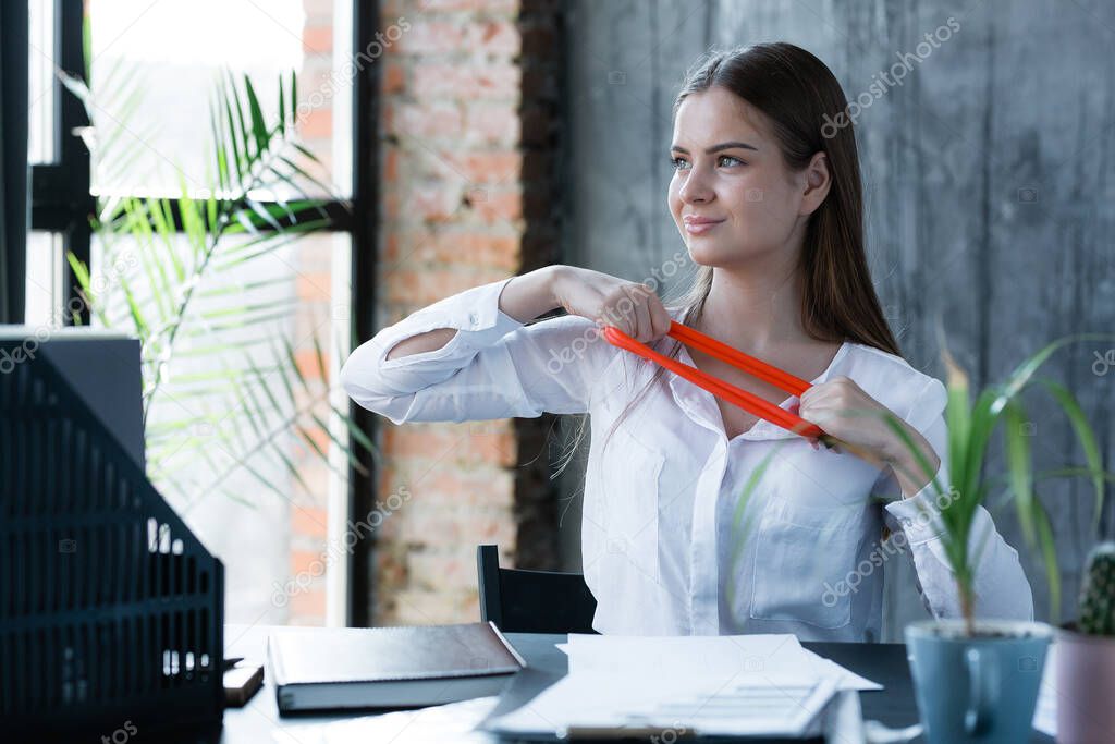 Happy French young girl during a work break does an exercise with a tape expander for back pain due to sedentary work