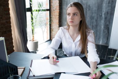 Beyaz gömlekli üzgün kız işten çıkarma başvurusunun önünde bir masada oturuyor ve işten çıkarma ve işsizliği düşünüyor..