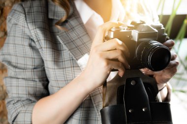 Kareli ceketli bir kadın, antika bir kamerayla fotoğraf çekiyor. Fotoğraftaki güneş ışınları.