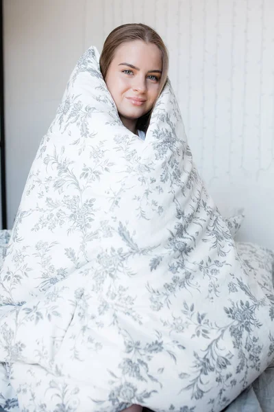 Una chica atractiva se sienta en la cama en una manta y disfruta de ropa de cama fresca y limpia — Foto de Stock