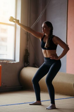 Spor üniformalı bir sporcu spor salonunda spor ağırlığıyla çömelir..