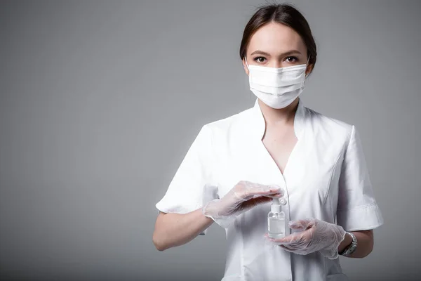 Médico estudante está em um casaco branco em uma máscara médica e óculos mantém um anti-séptico nas mãos sobre fundo branco durante uma pandemia — Fotografia de Stock