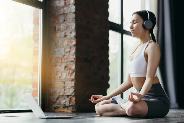 Entrenador asiático de yoga medita con música relajante en auriculares y vídeo en portátil en estudio — Foto de Stock