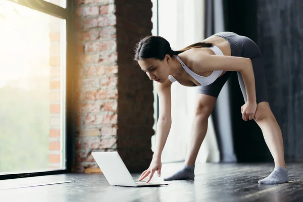 Fata asiatică este angajată în stretching. Înclinări cu un plat înapoi la laptop pentru a vă conecta la lecție — Fotografie, imagine de stoc