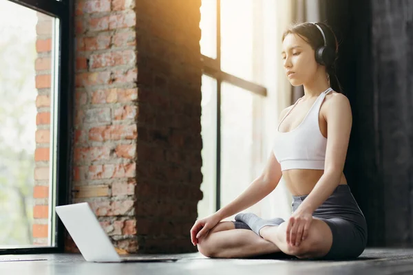 Meditând în poziția de lotus în fața unui laptop online. Fata din căști face yoga — Fotografie, imagine de stoc