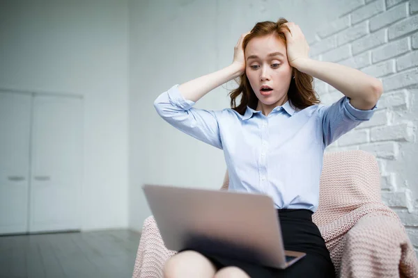 Chica pelirroja sostiene sus manos detrás de su cabeza y aturdido en la pantalla del ordenador portátil mientras está sentado en un sillón en un traje de negocios — Foto de Stock
