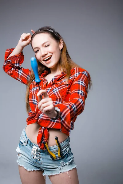 Gelukkig meisje in een rood shirt met een schroevendraaier op een grijze achtergrond. Reparatie- en bouwconcept — Stockfoto