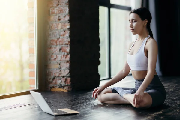 Mujer sentada en posición de loto en un brillante studio.Engaged en el entrenamiento en línea porque el gimnasio está cerrado debido coronavirus — Foto de Stock