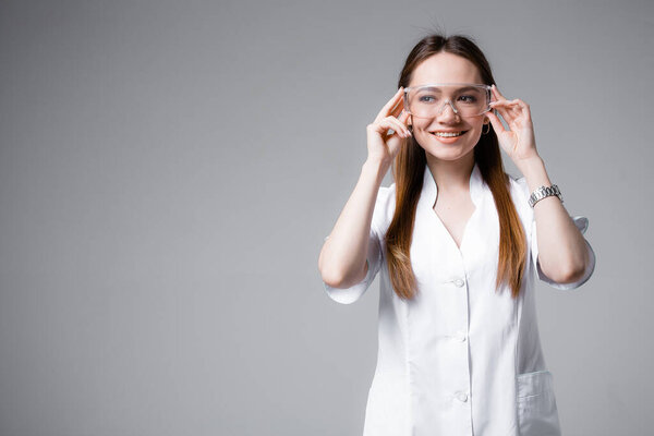 English doctor in a white medical coat and goggles stands and smiles on a gray background